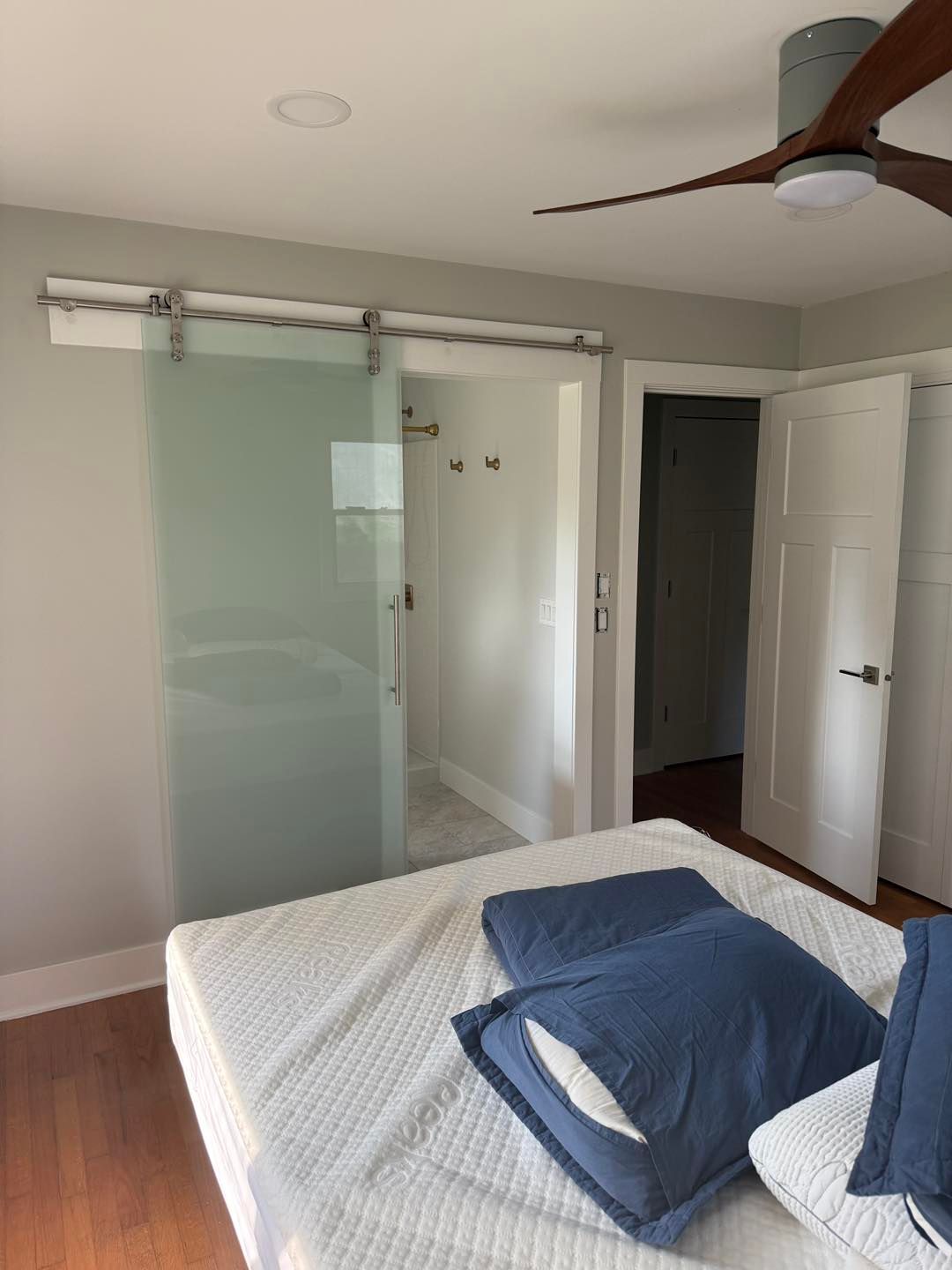 Bedroom with a bed, blue pillows, frosted sliding closet doors, and an open doorway to a hallway.