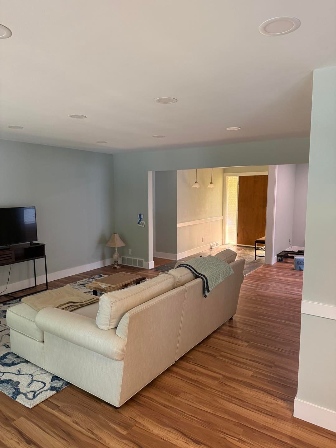Living room with a white sofa, TV, rug, and open doorway to a lit hallway