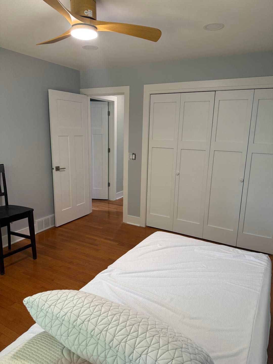 Small bedroom with white closet doors, open doorway, wood floor, and unmade bed under a ceiling fan.