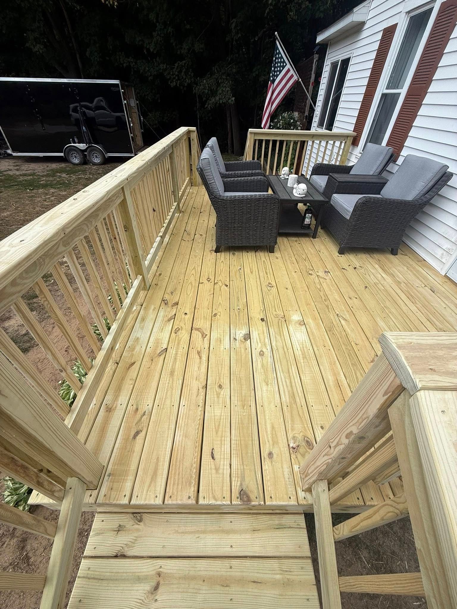 Wooden deck with railings, wicker chairs, gray cushions, and an American flag at night