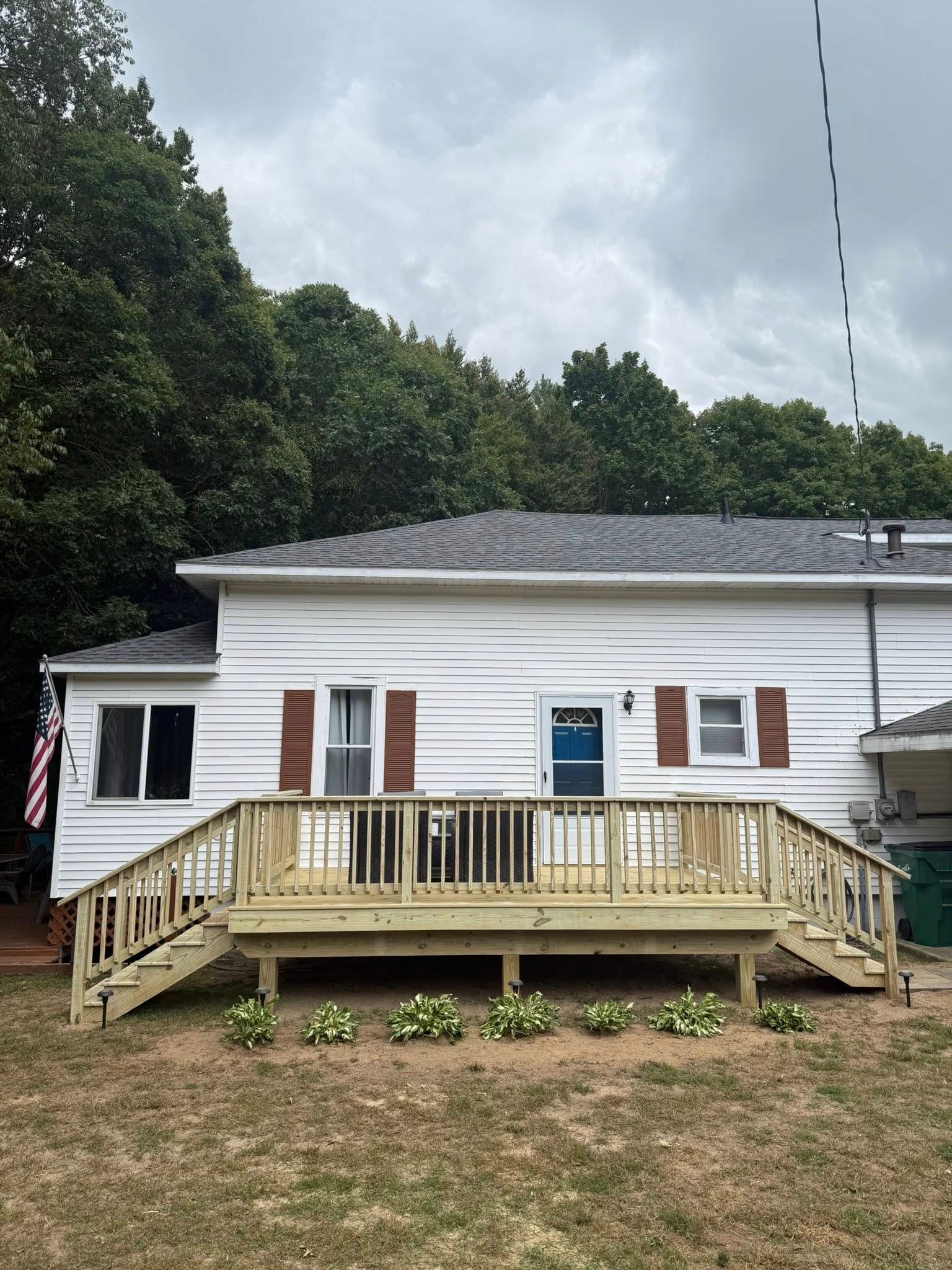 White house with a wooden front porch and steps, set on a grassy lot under cloudy skies.