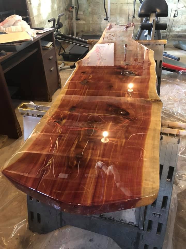Glossy live-edge wooden tabletop on saw horses in a workshop, with rich reddish-brown grain.