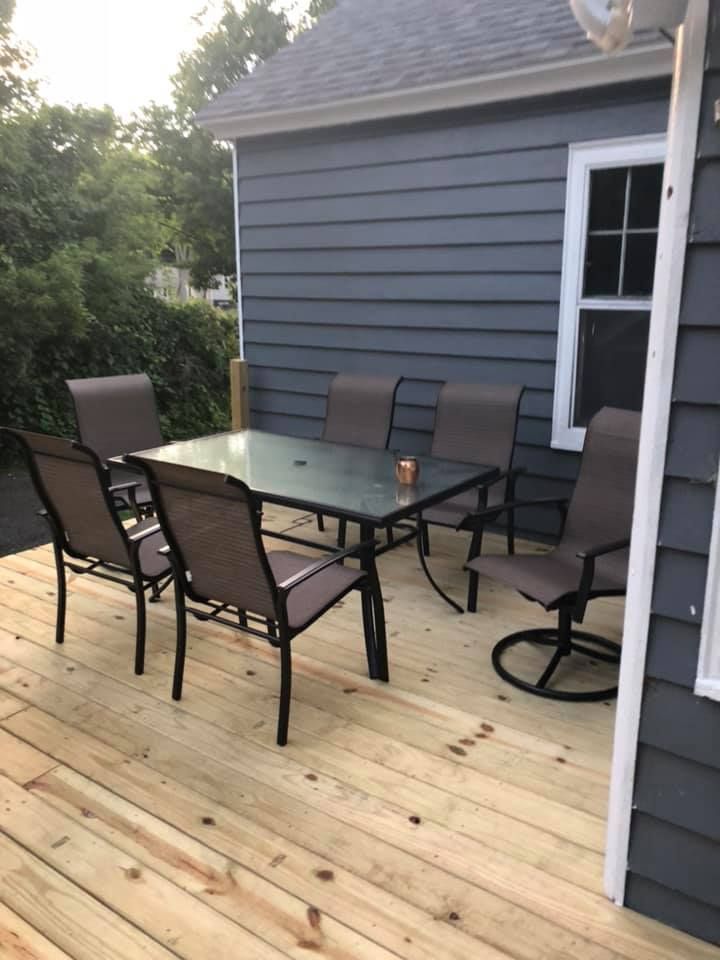 Outdoor wooden deck with black patio table and chairs beside a gray house.