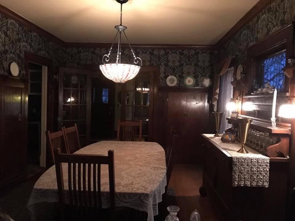 Dining room with floral wallpaper, wooden table, chairs, chandelier, and sideboard under warm lighting.