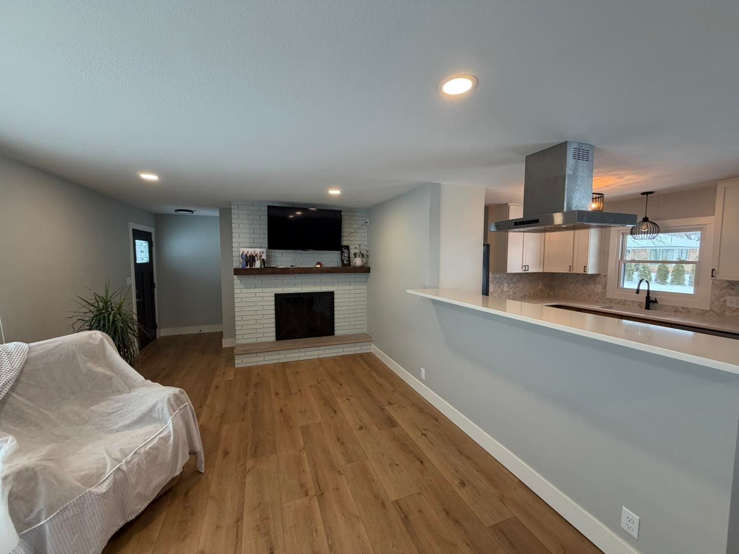 Empty living room with hardwood floors, fireplace, TV, and open kitchen pass-through.