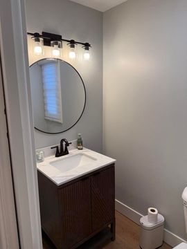 Small bathroom vanity with round mirror, wall lights, white sink, and toilet paper holder.