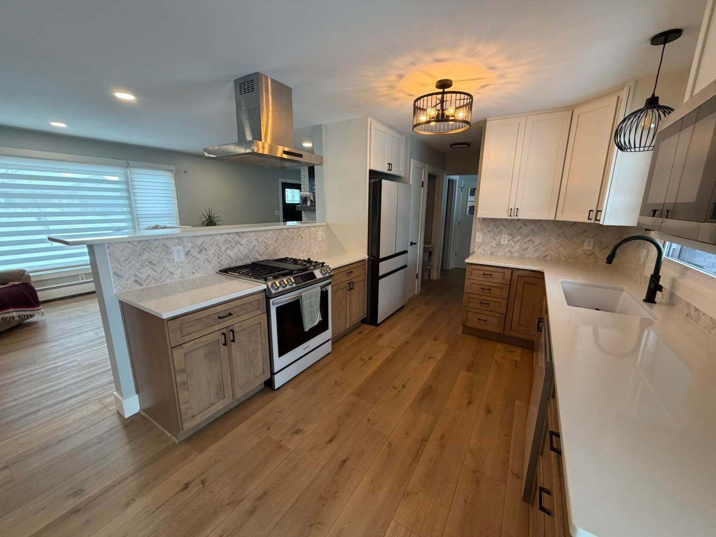 Bright modern kitchen with white cabinets, wood floors, island, stainless appliances, and large window
