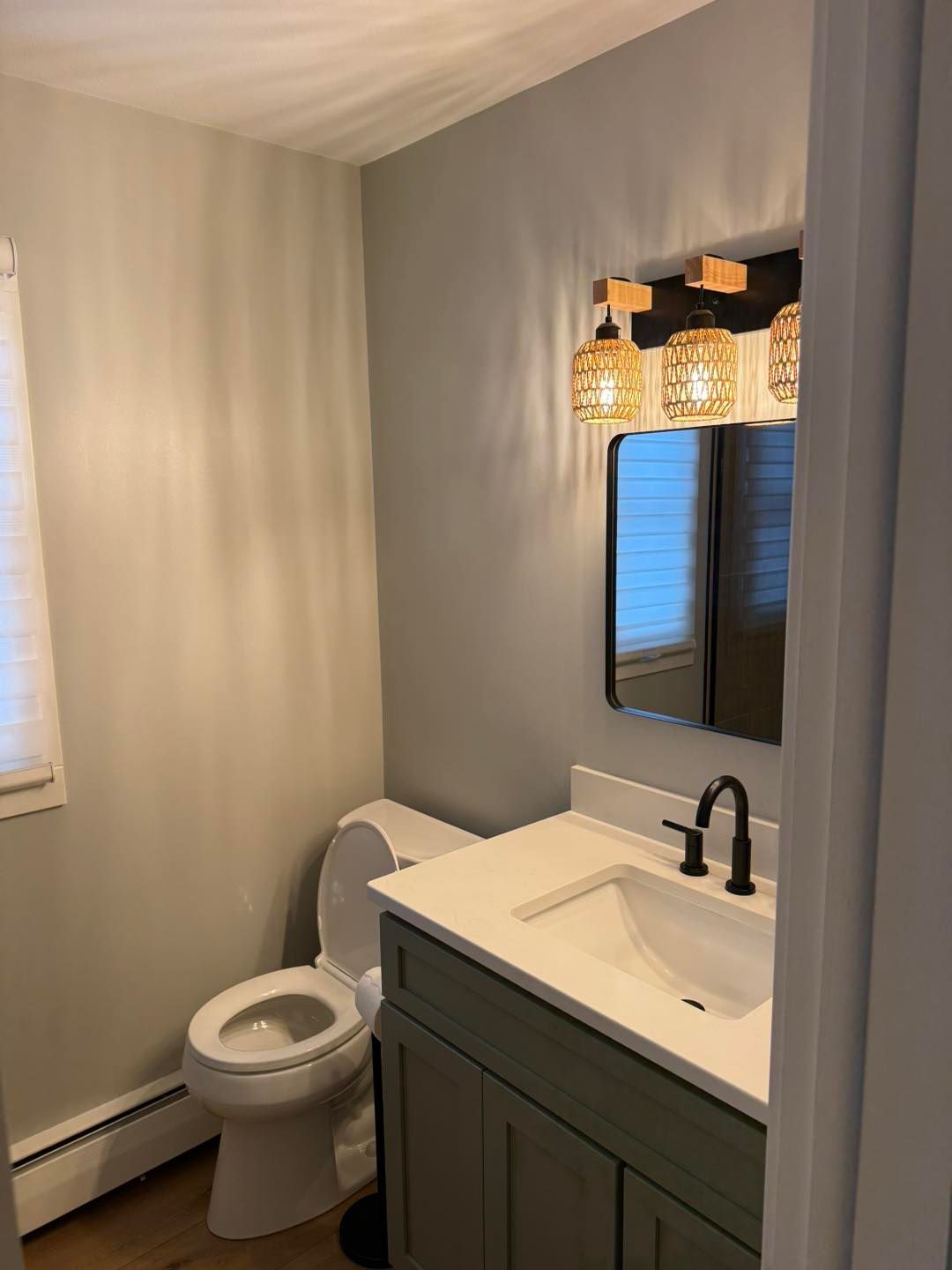 Small bathroom with gray walls, toilet, vanity sink, black faucet, mirror, and hanging pendant lights