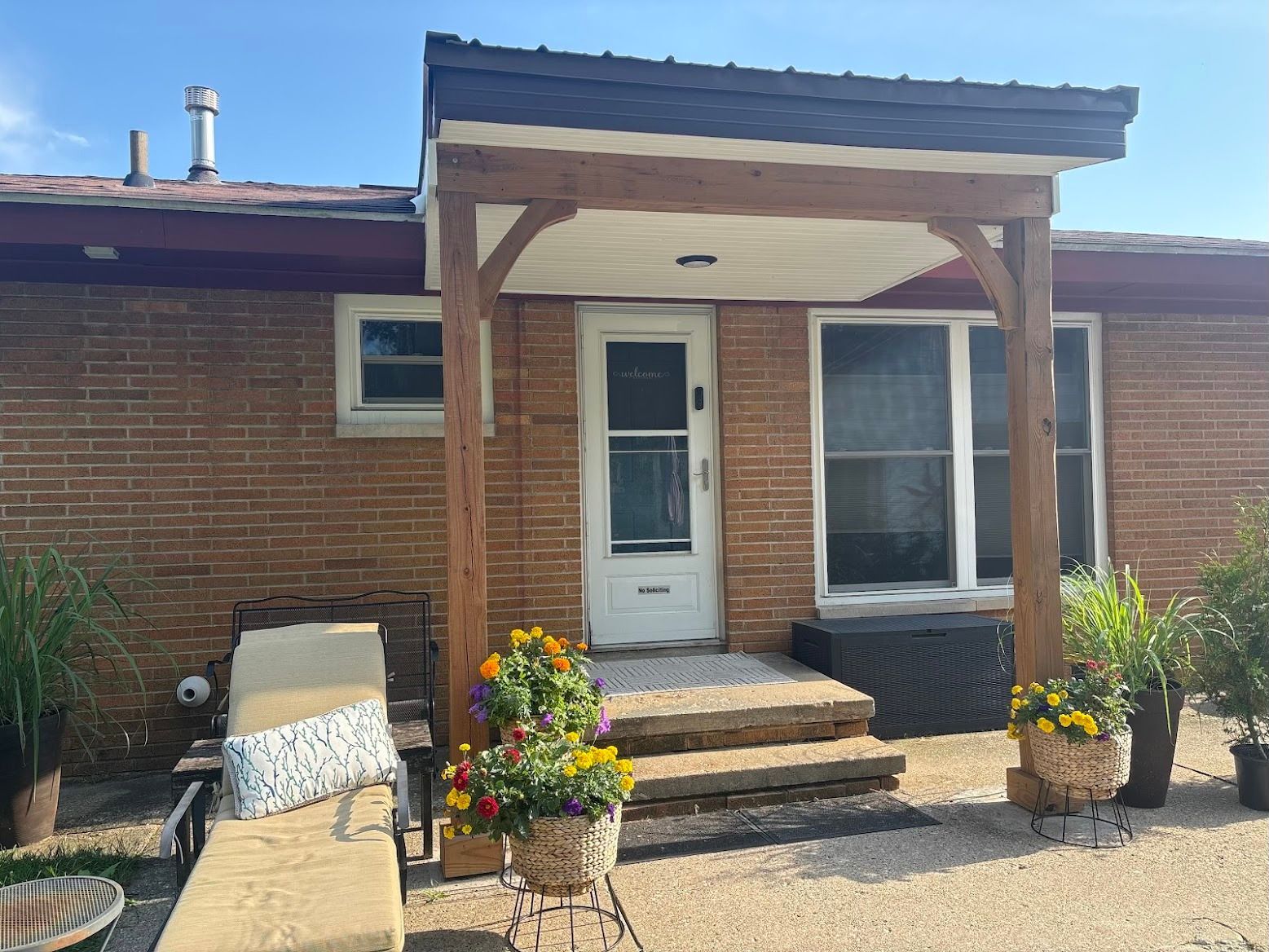 Brick house entry with wooden porch, steps, potted flowers, and a white front door