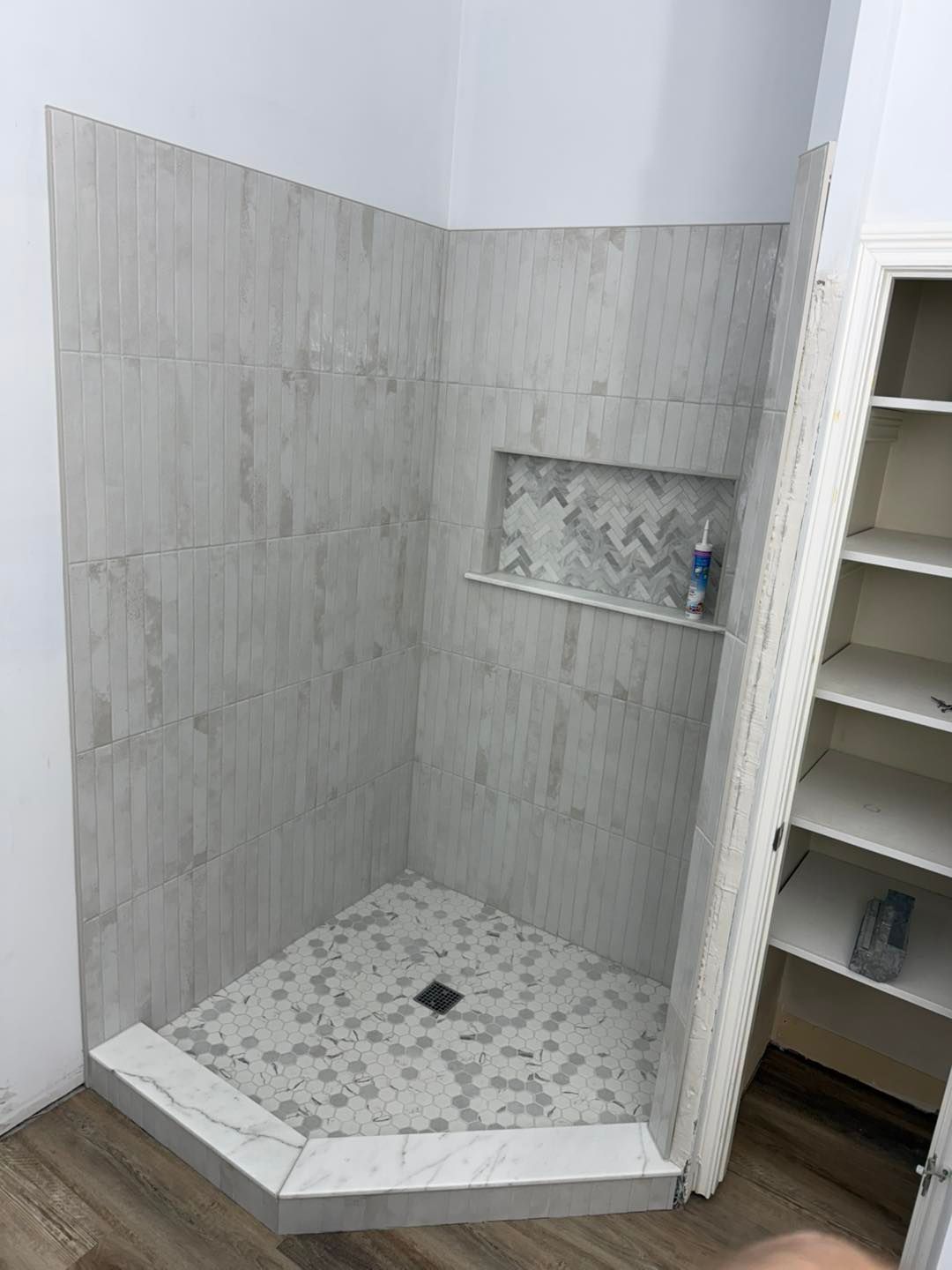 Walk-in tiled shower with built-in shelf and hexagonal floor tiles in a bathroom.