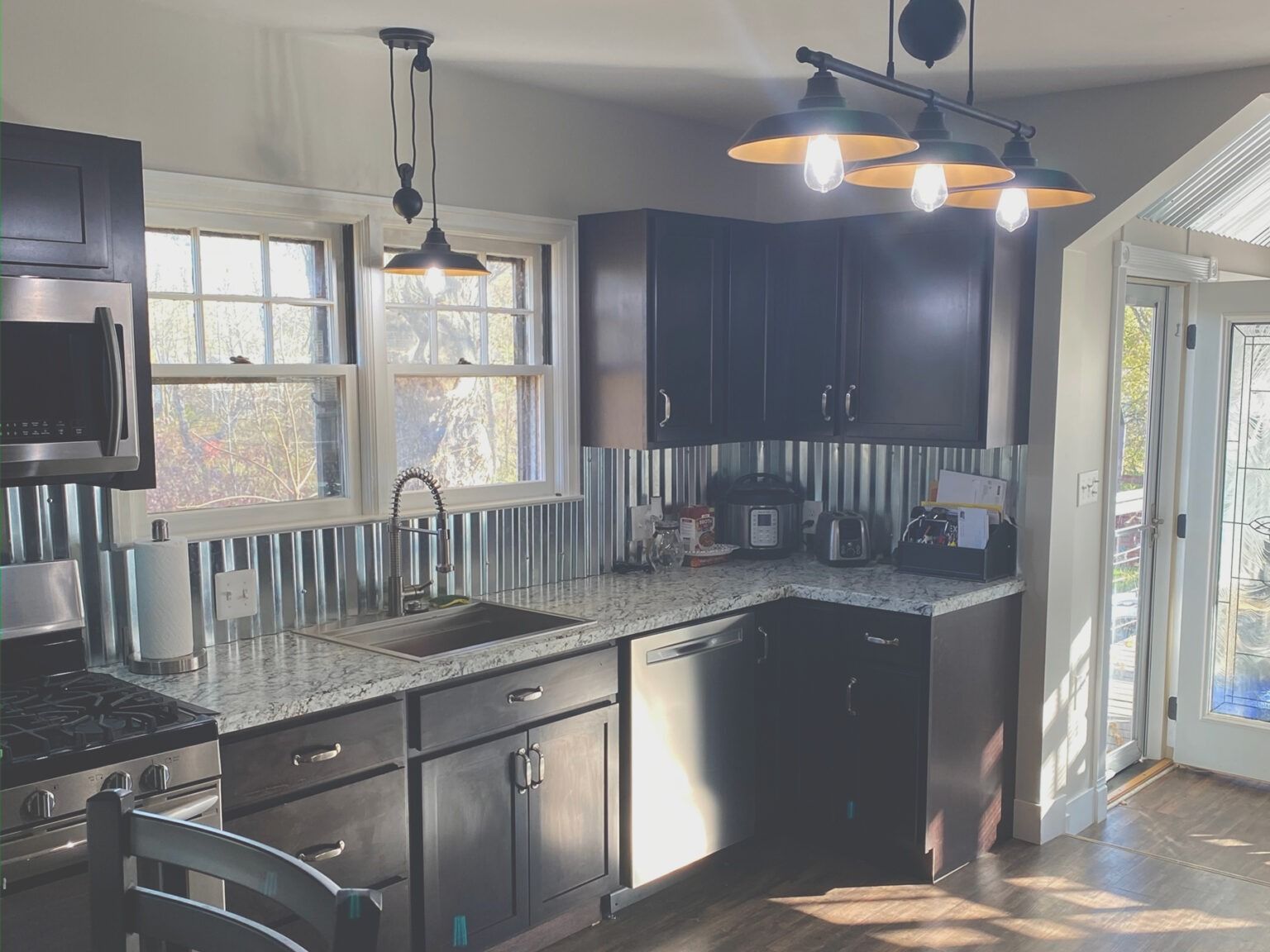 Modern kitchen with dark cabinets, granite counters, stainless appliances, and an open glass door to outside