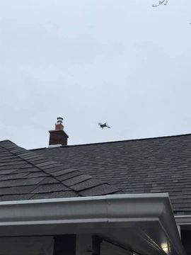 Drone flying above a house roof near a chimney against a cloudy sky