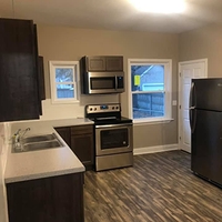 Modern kitchen with stainless steel appliances, dark cabinets, light counters, and two windows