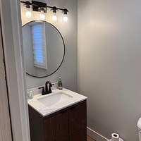 Small modern bathroom vanity with round mirror, black light fixture, and white sink.