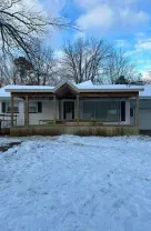 Snow-covered single-story house with a porch under a blue winter sky