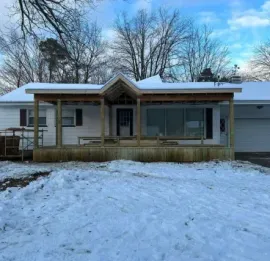 Snow-covered house with a porch and garage under a blue sky