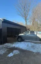 Gray pickup truck beside an open metal garage on a snowy driveway under a clear blue sky