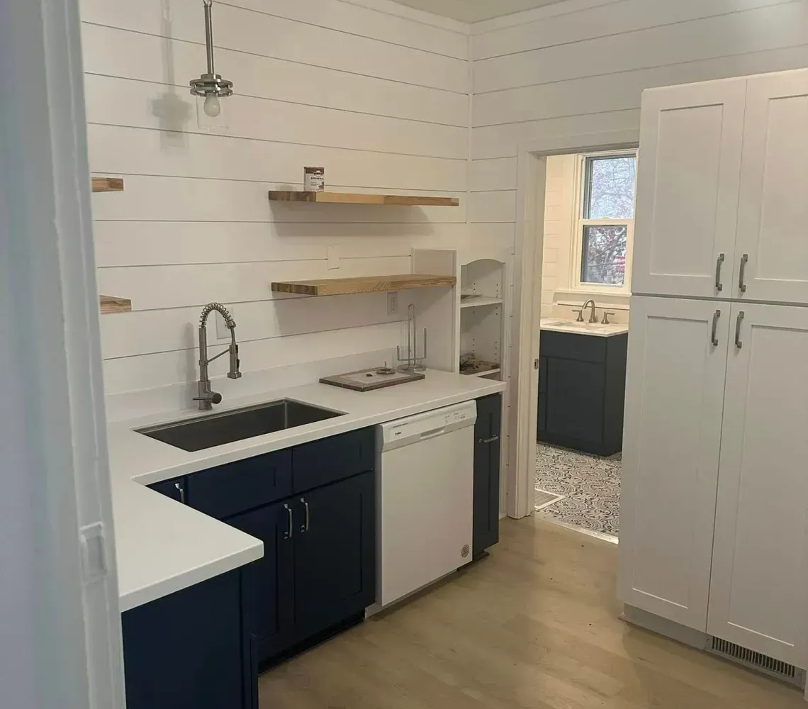 Small kitchen with white cabinets, wood floors, open shelves, and a doorway to another room.