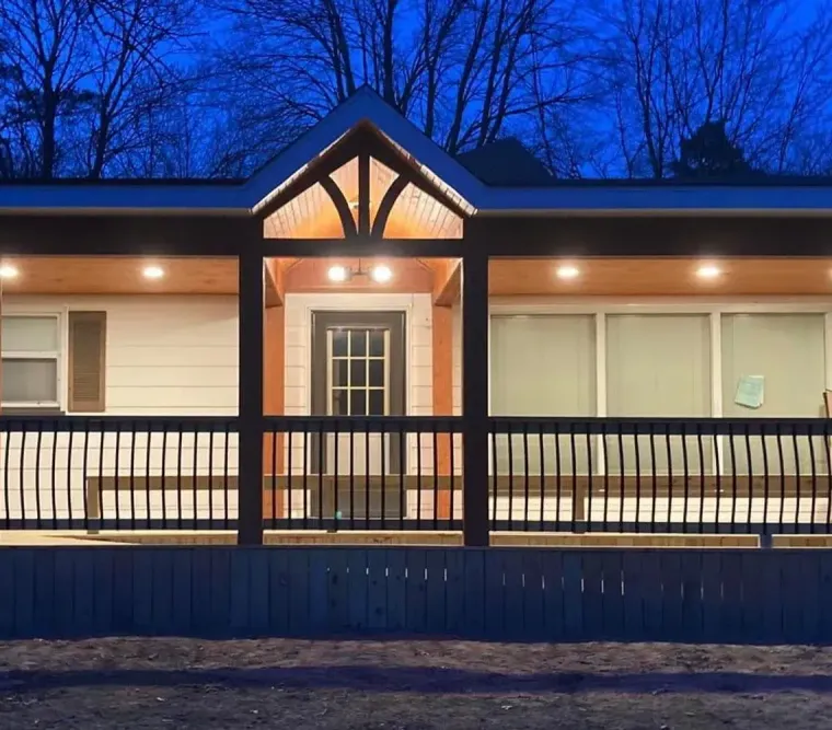 Front view of a lit house at dusk with a covered porch and wooden railings