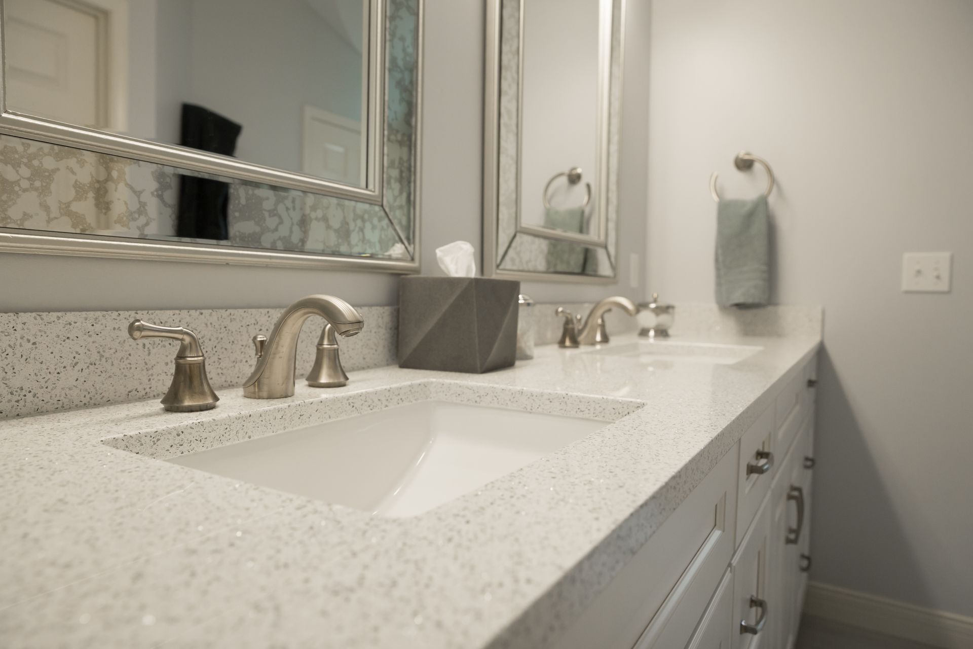 Bathroom with double sinks, light countertops and cabinets, mirrors, and silver fixtures.