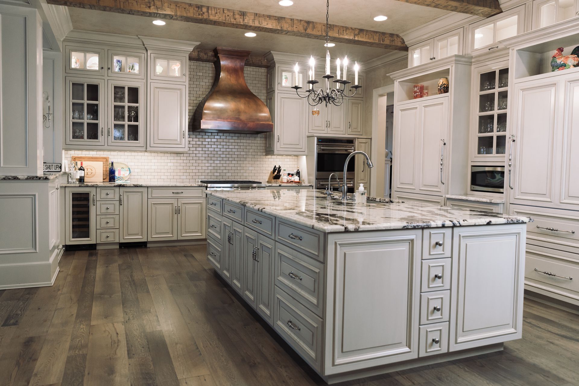 Elegant white kitchen with large island, copper hood, and hardwood floors.