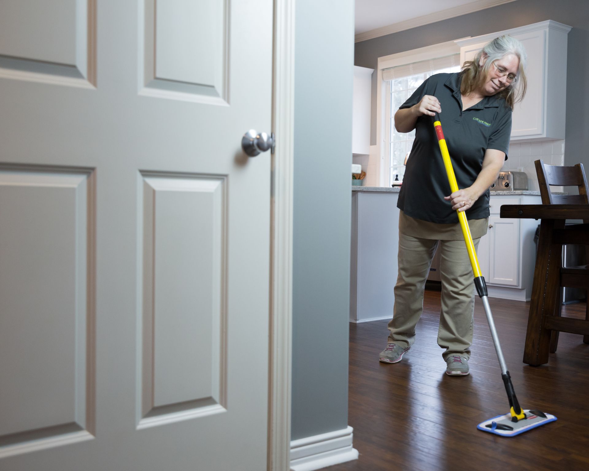 Woman mopping a wooden floor inside a house, near a closed white door.