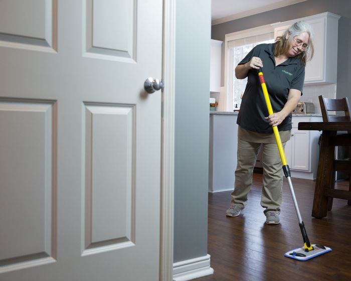 Woman mopping a wooden floor inside a house, near a closed white door.