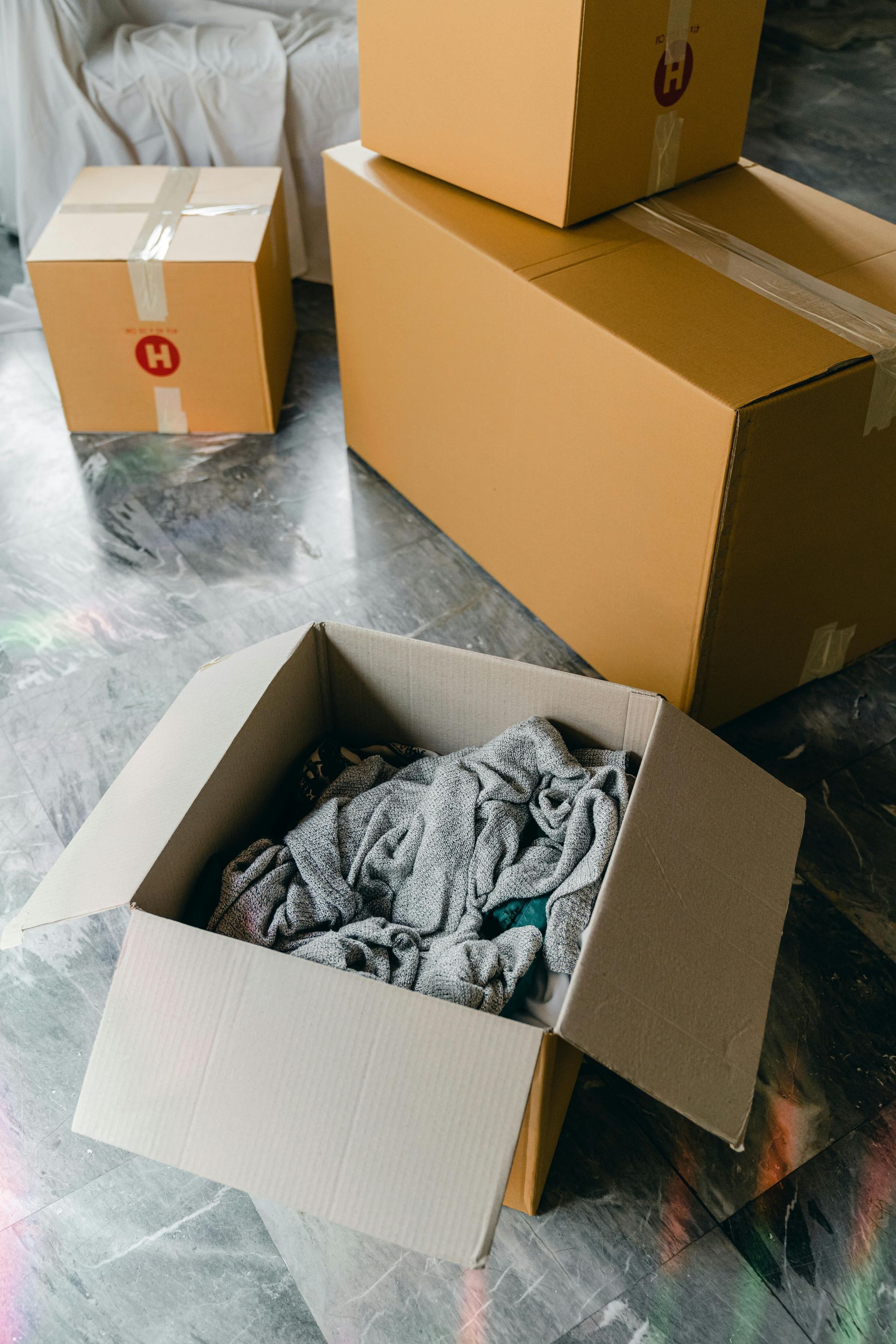 Cardboard boxes, one open with clothing, on a concrete floor, ready for moving.