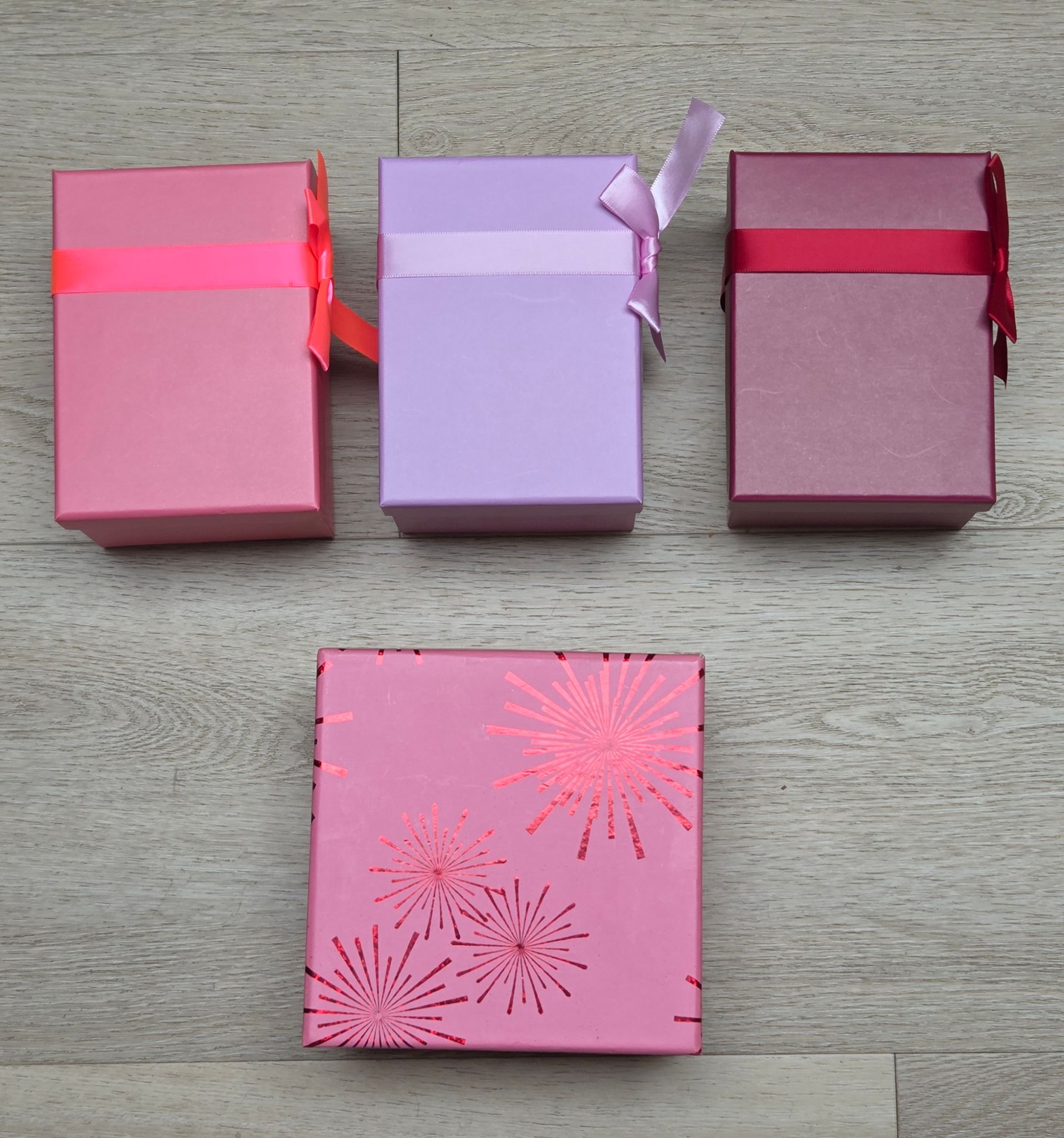 Vier kleine pastelkleurige geschenkdoosjes staan ​​op een houten ondergrond, met daaronder een roze doosje met patroon.