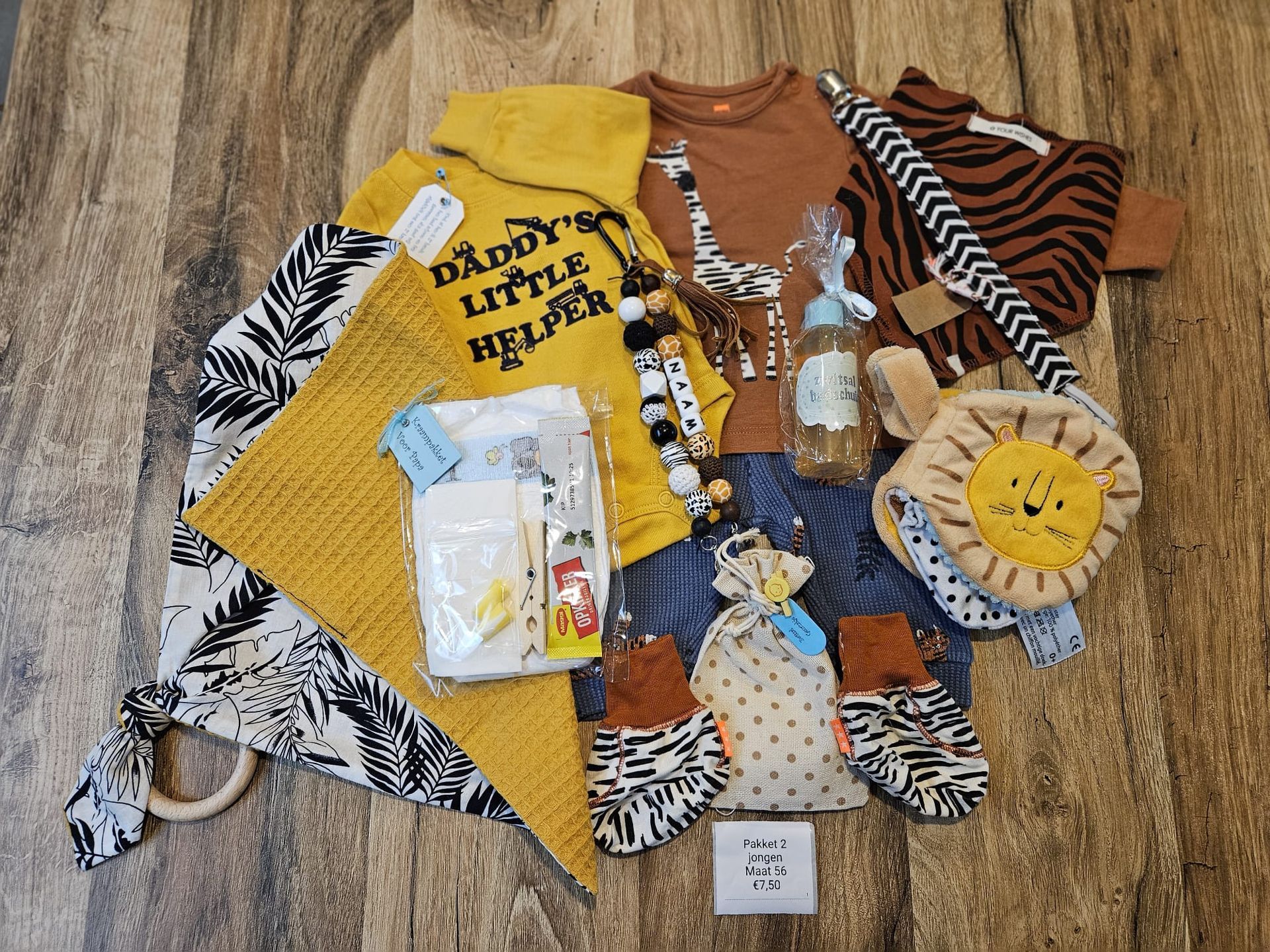 Kinderkleding en accessoires uitgestald op een houten vloer, waaronder een geel shirt, kleding met zebraprint en een zontas.