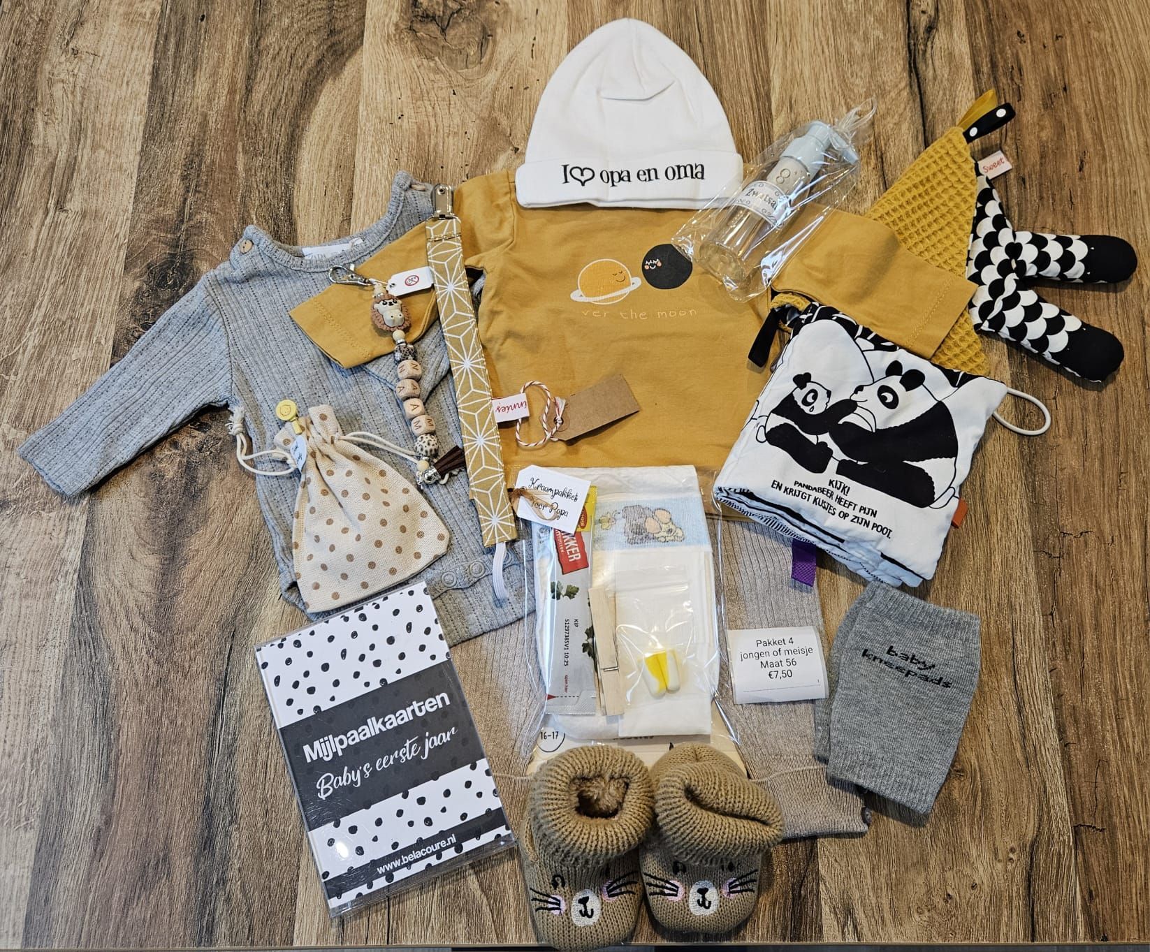 Een platte legging van babykleding en -accessoires in grijs, mosterdgeel en zwart-wit op een houten vloer.