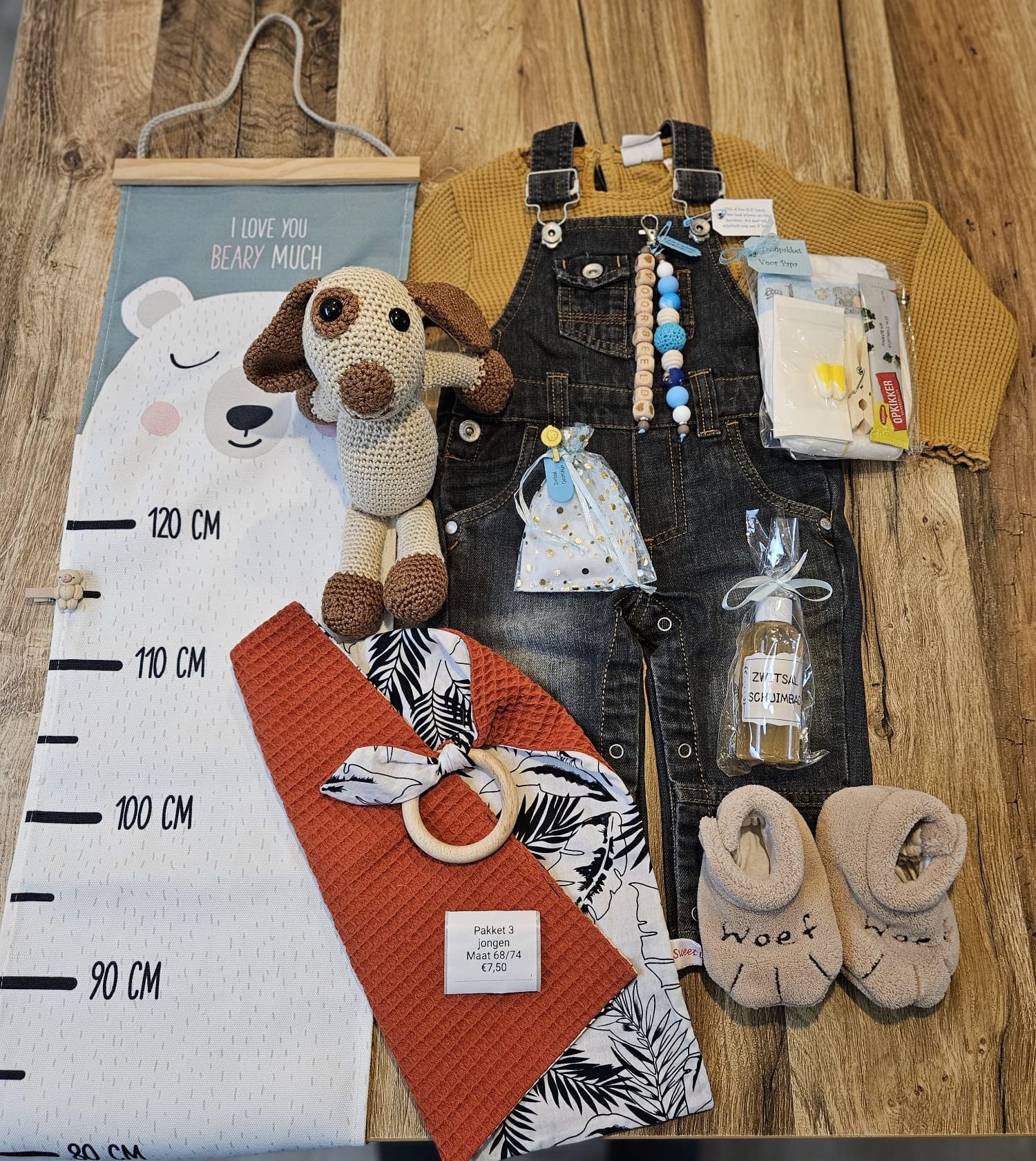 Babykleding en accessoires die passen bij de mijlpalen van een mijlpaal liggen uitgestald op een houten vloer naast een grijze groeimeter.