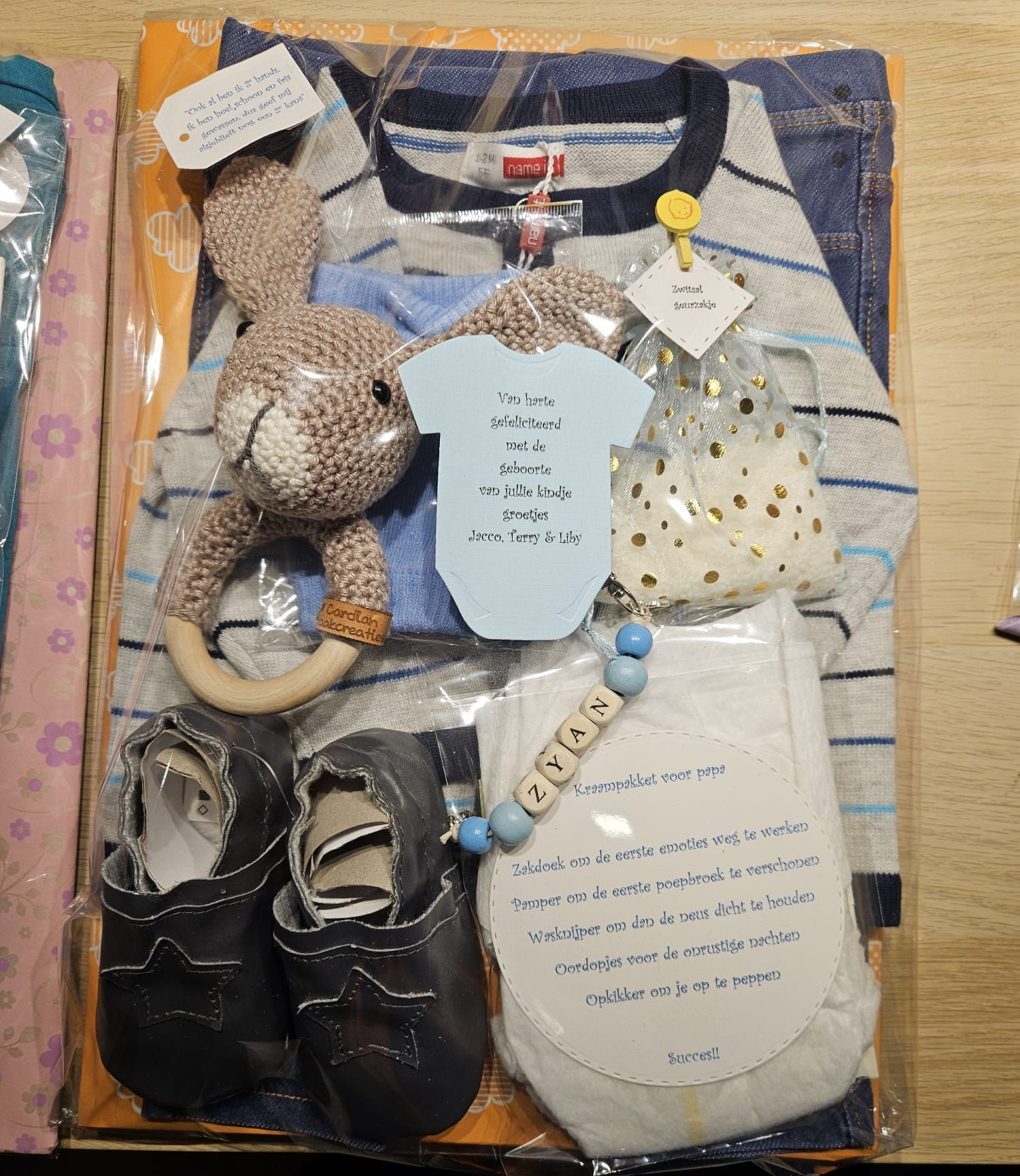 Een sprei met diverse babycadeautjes, waaronder een gestreept rompertje, een gehaakt speeltje, schoentjes, slabbetjes en een flessentas.