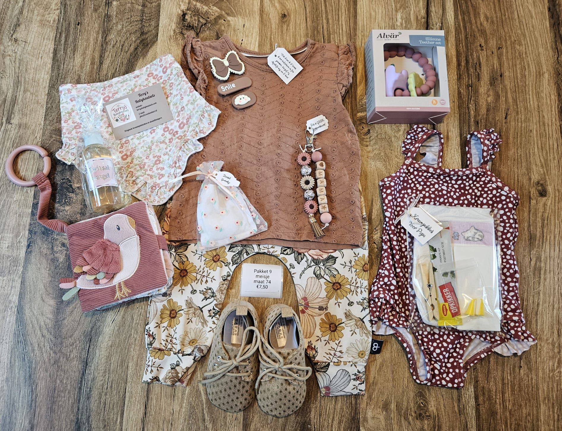 Diverse babykleertjes, accessoires en aandenken liggen plat uitgestald op een houten vloer.