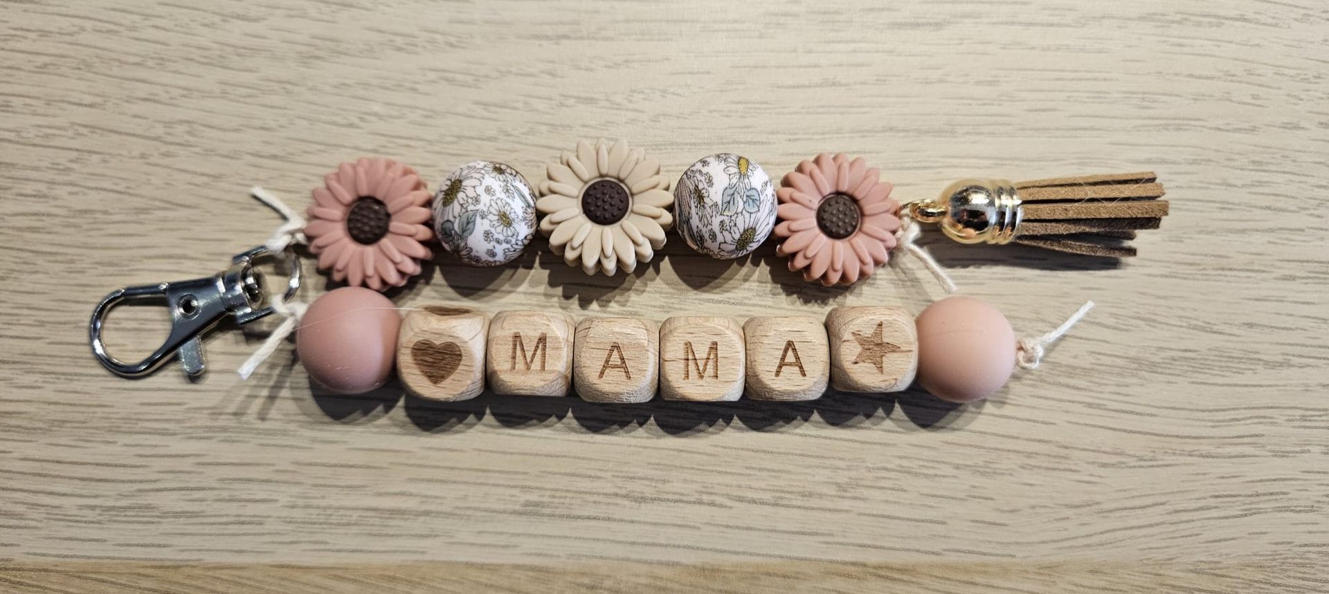 Roze en crèmekleurige kralen sleutelhanger met kwastje en gegraveerde houten kralen op een houten ondergrond