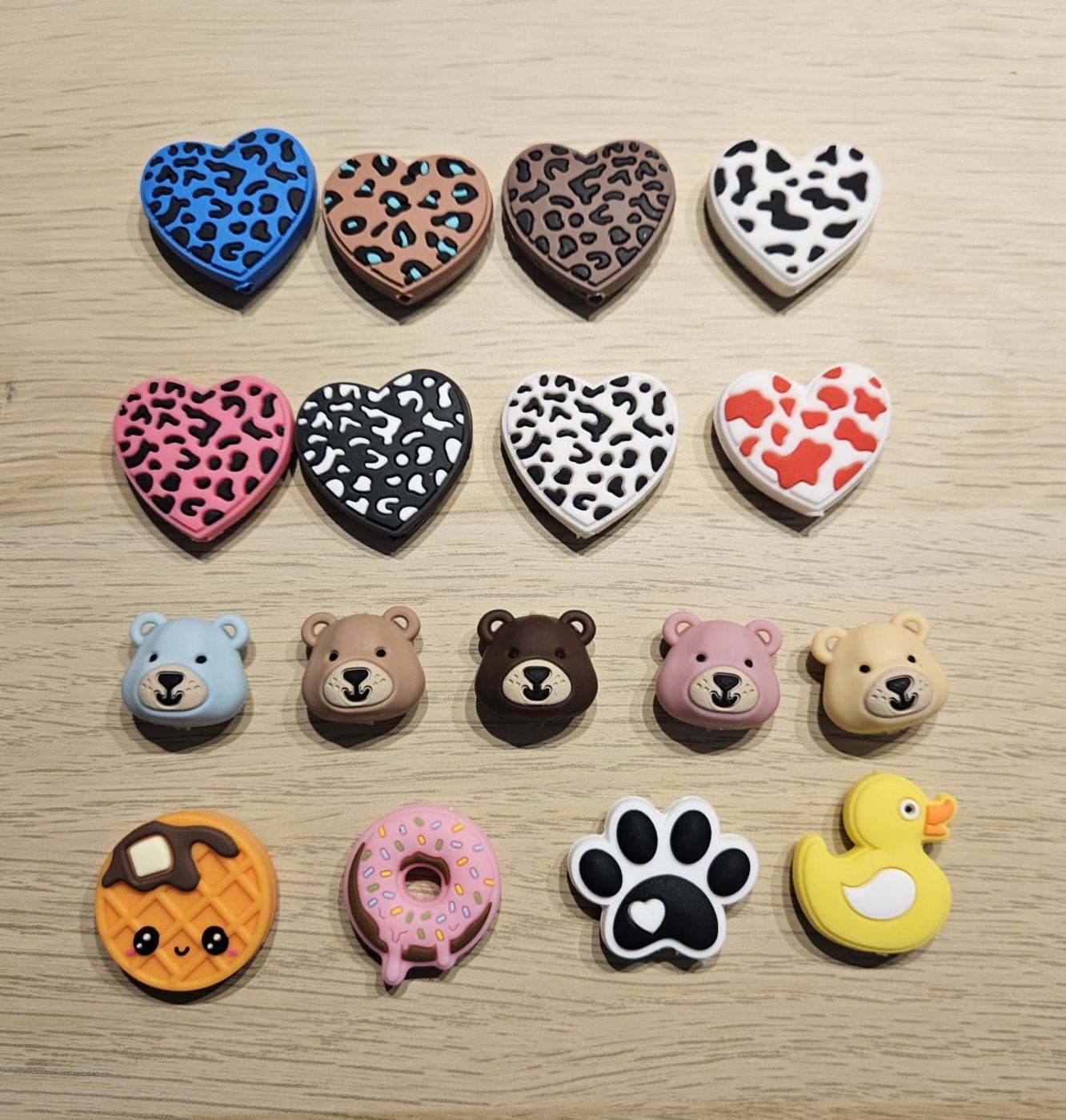 Diverse bedeltjes met dierenprint en pastelkleurige accessoires in de vorm van beren, pootafdrukken, pompoenen, donuts en eenden, netjes in rijen gerangschikt.
