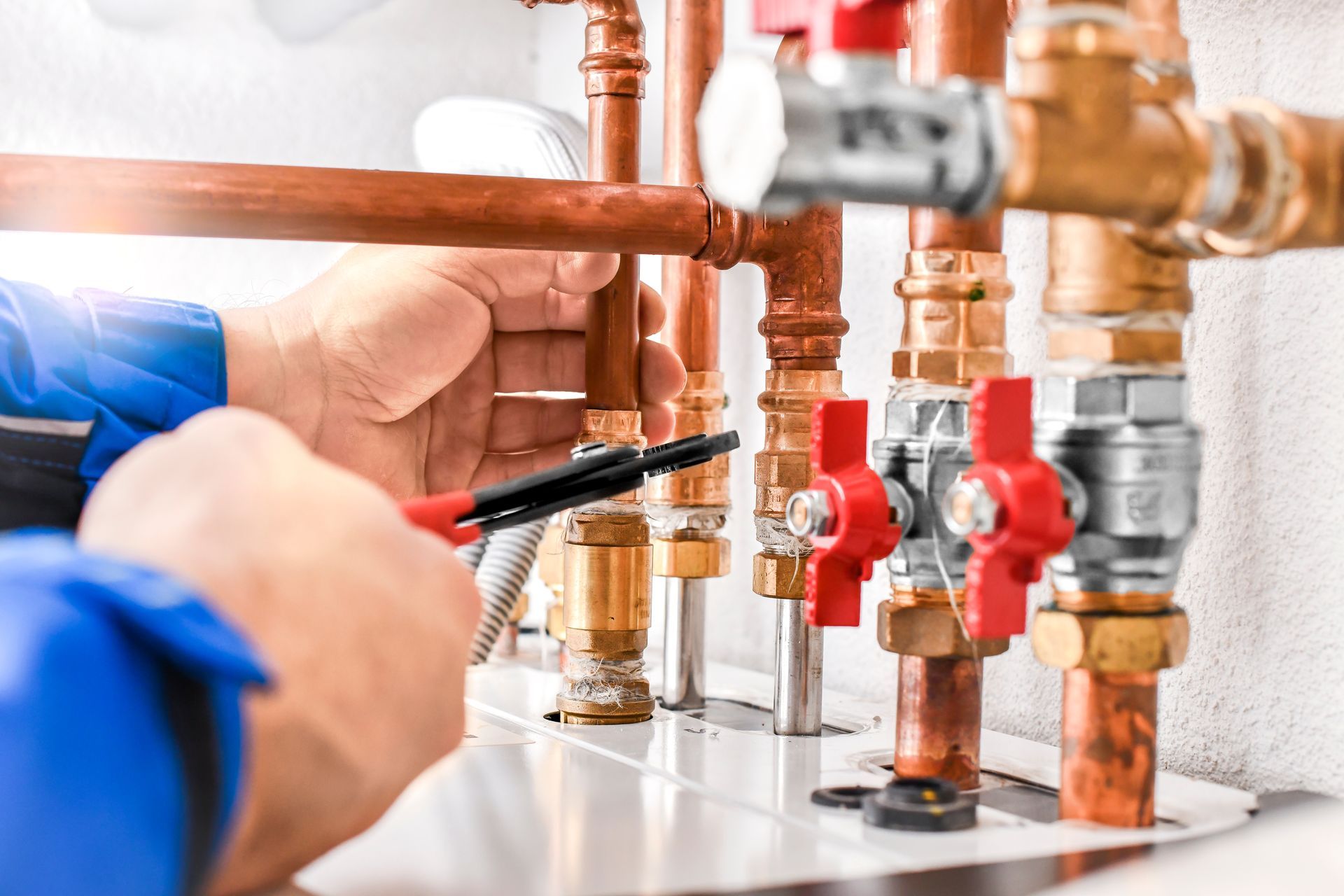 Plumber tightening copper pipes with a wrench on a white wall-mounted plumbing manifold
