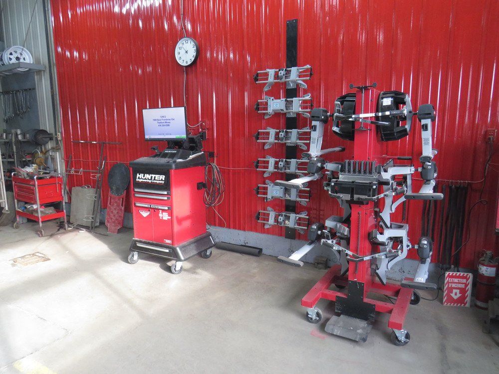 Un appareil de réglage de la géométrie des pneus rouge dans un garage aux murs rouges. Une armoire à outils et des outils sont visibles.