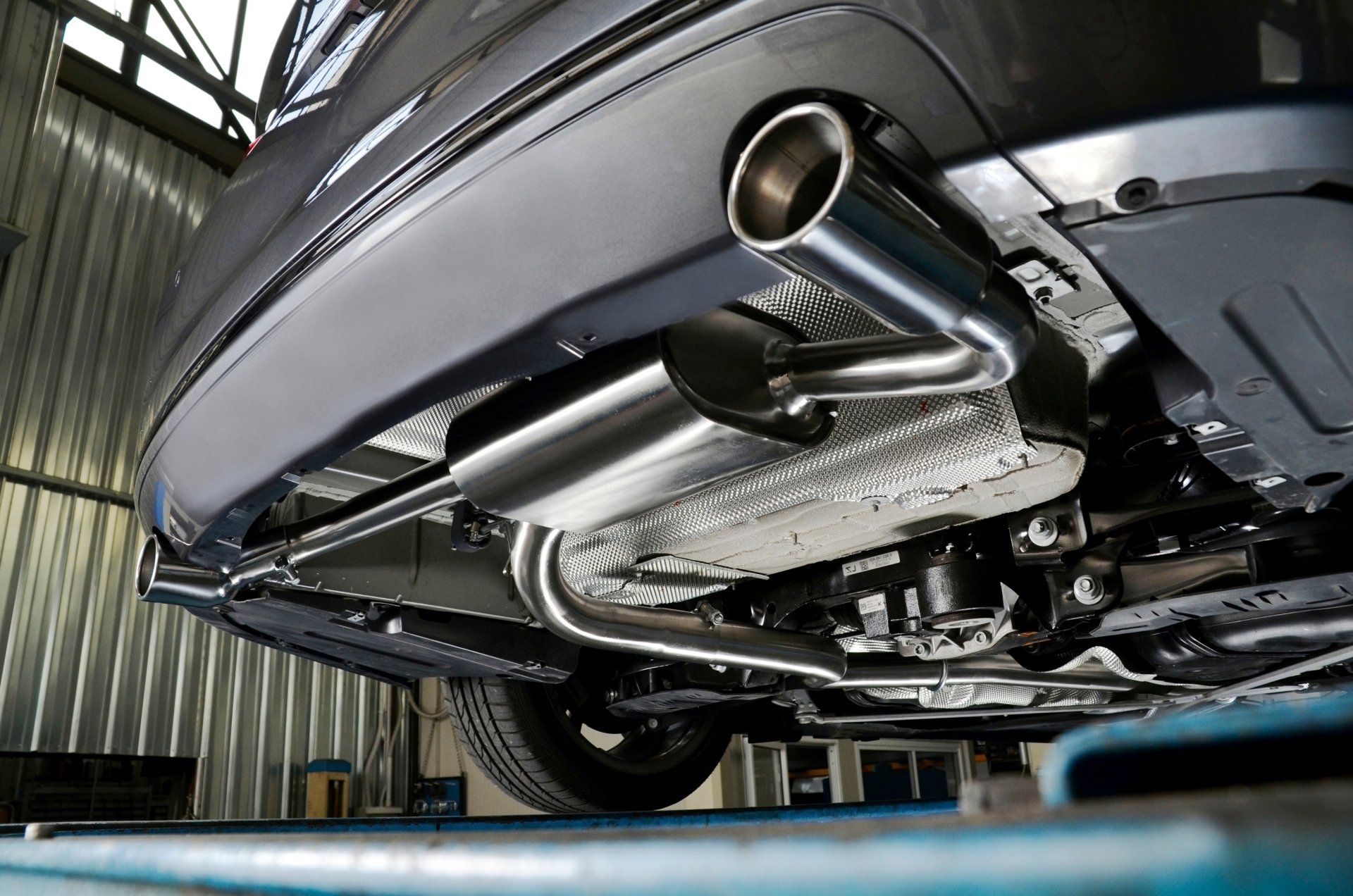 Châssis d'une voiture grise avec système d'échappement en acier inoxydable dans un atelier de réparation.