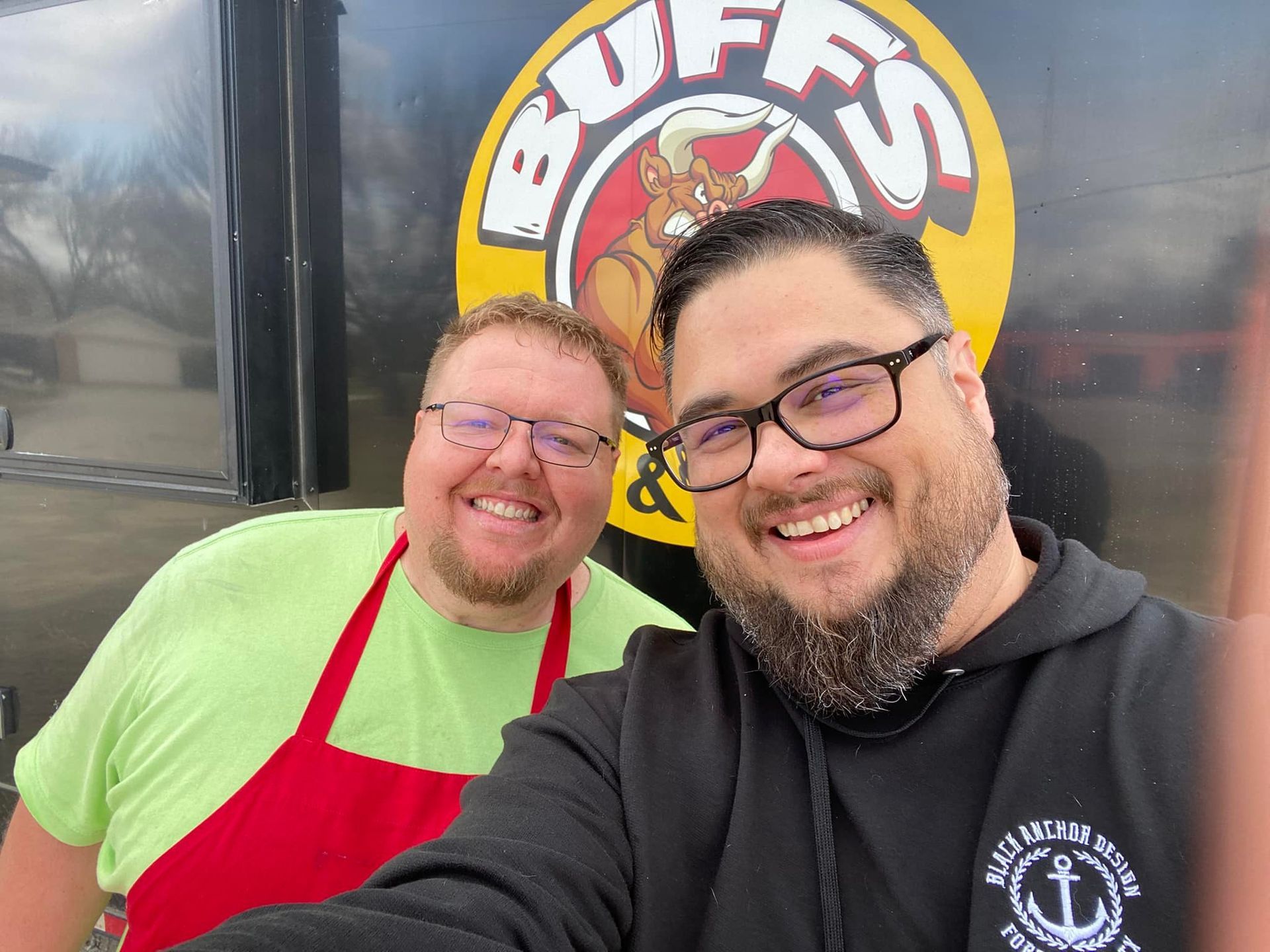 Two men are posing for a picture in front of a food truck.