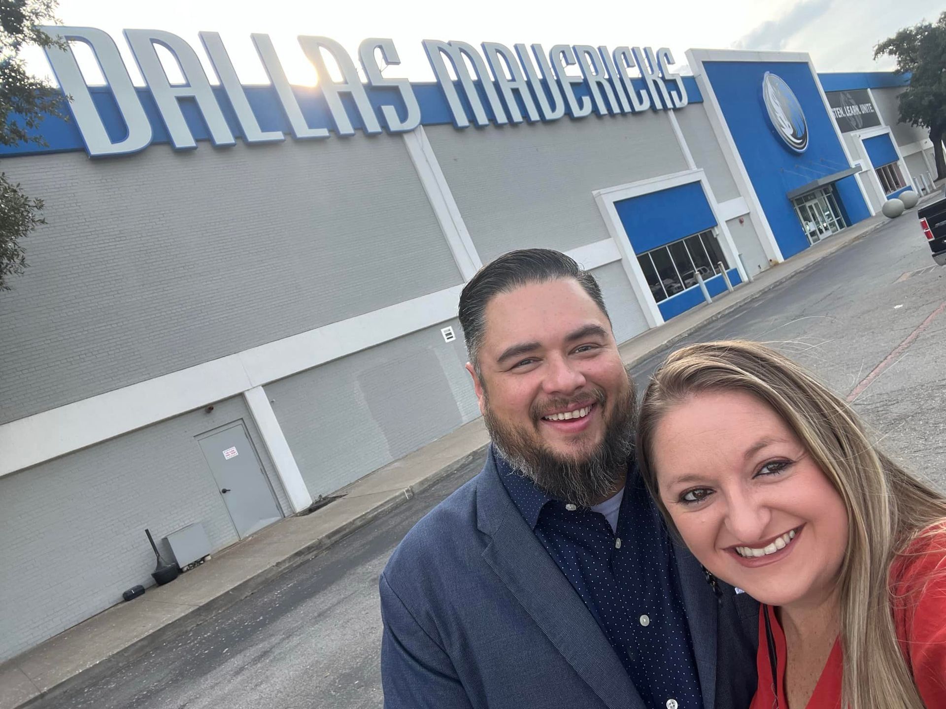 A man and a woman are posing for a picture in front of a dallas rams building.
