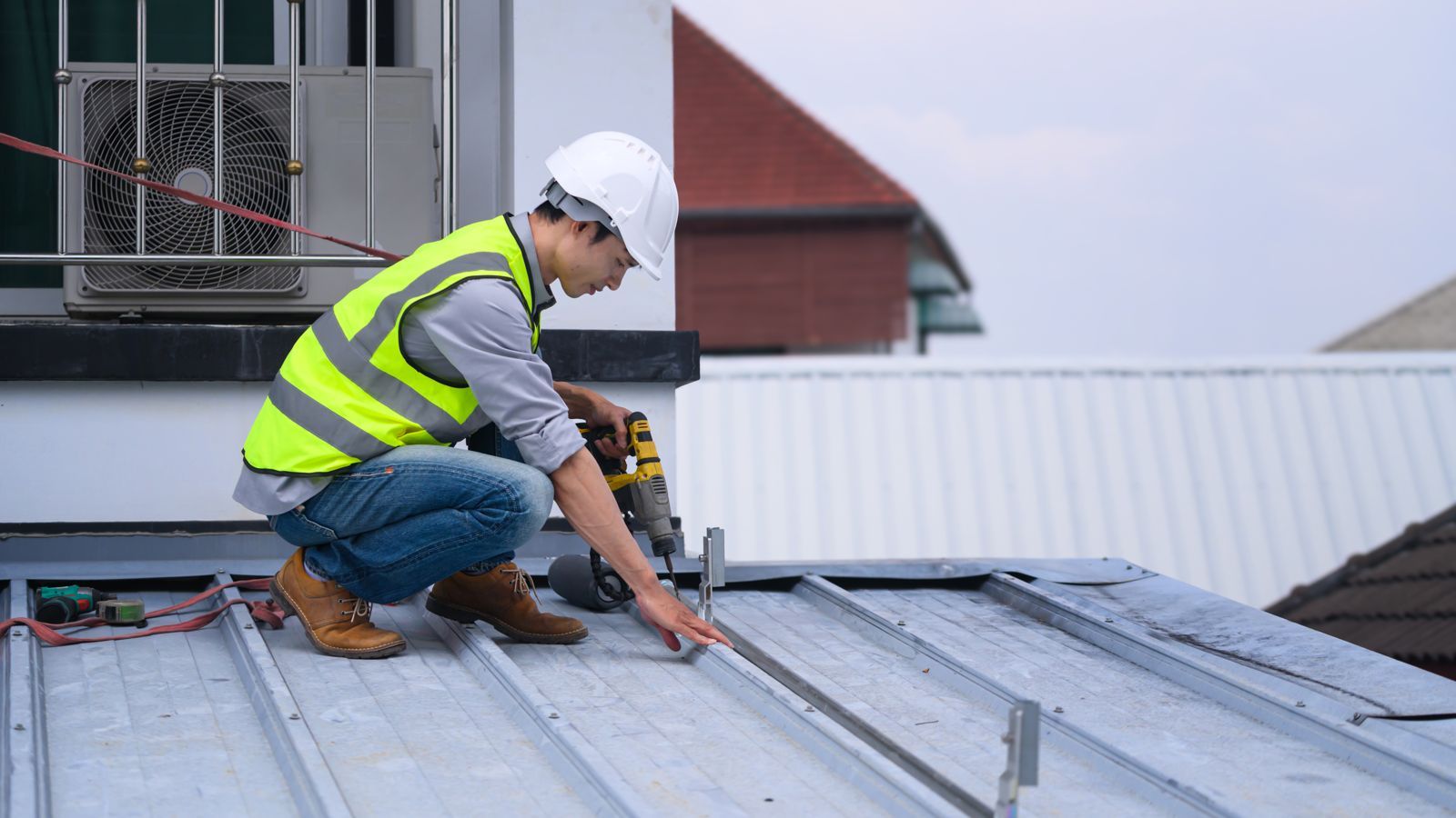 Commercial roofing worker installing metal roof panels with a power drill