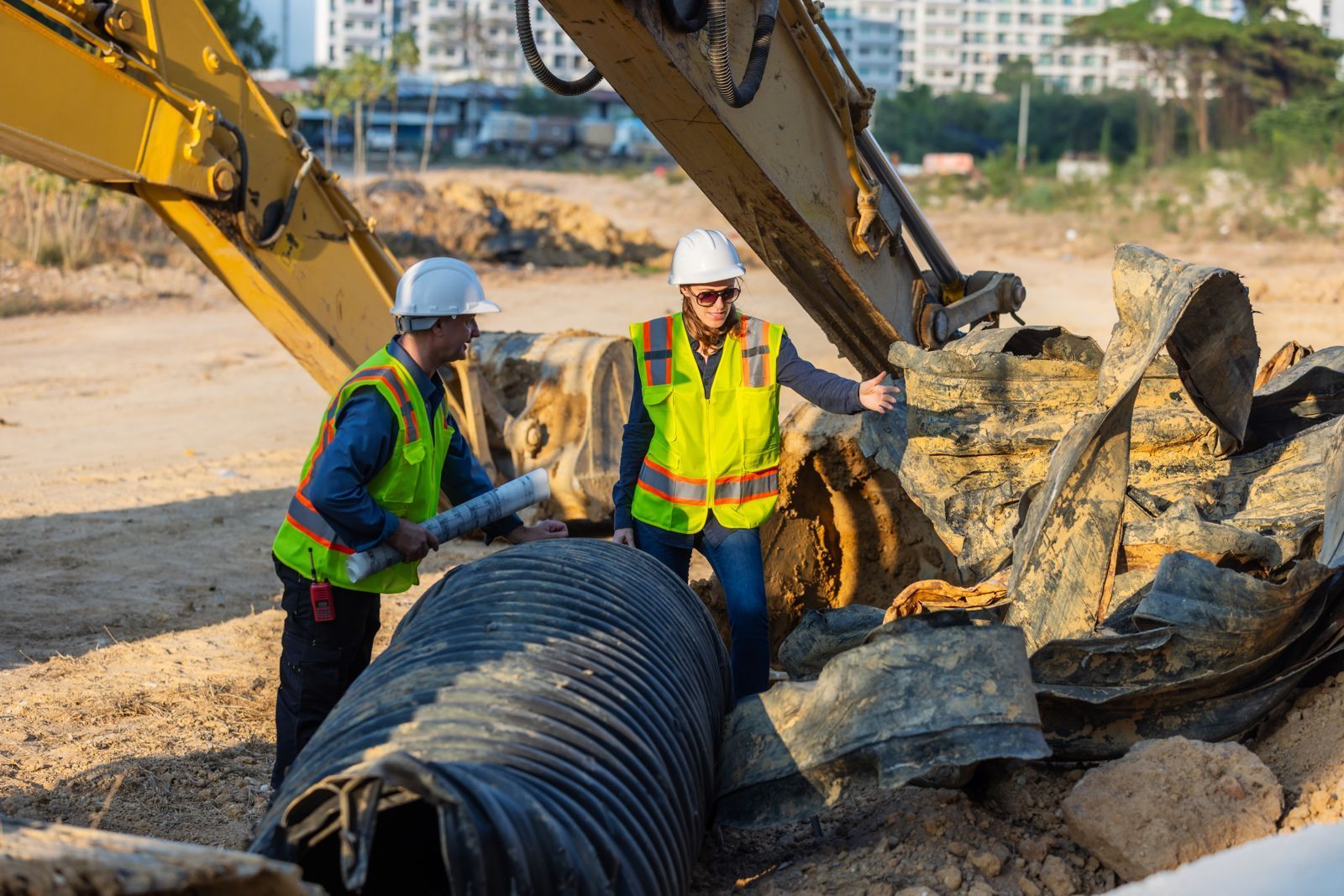 Utility crew inspecting pipe beside an excavator on a job site