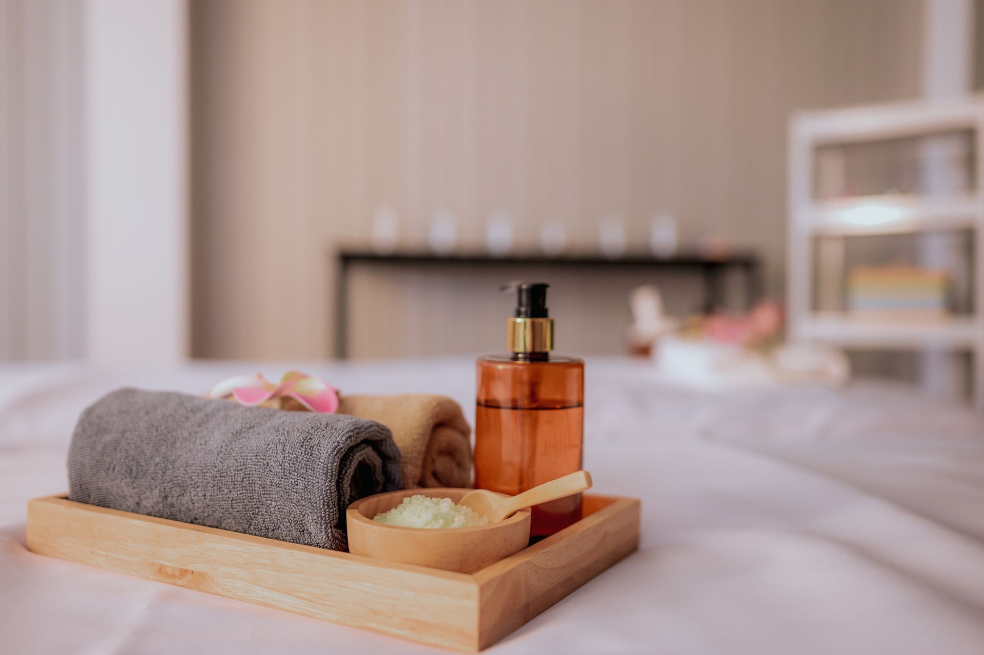 Un vassoio di legno con asciugamani, una bottiglia di lozione e una ciotola di sale su un letto.