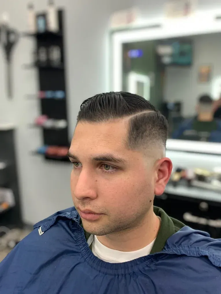Man with a sharp, faded haircut, styled side part, in a barber shop.