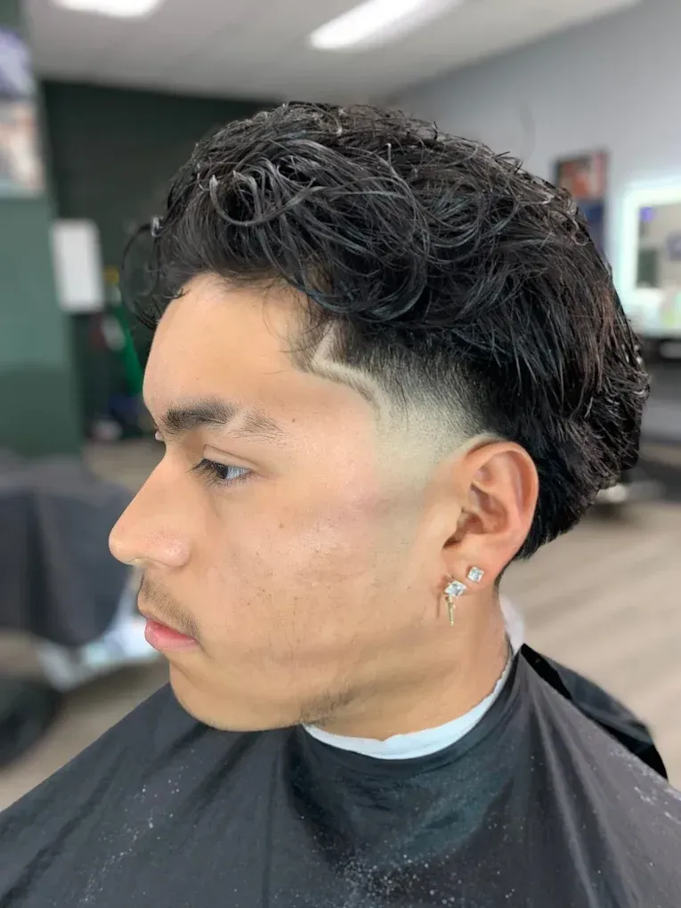 Man with a faded haircut, styled with curls, and a hairline design, in a barbershop.