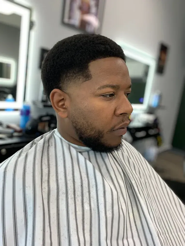 Man in barber cape with a tapered haircut, short beard, in a salon.