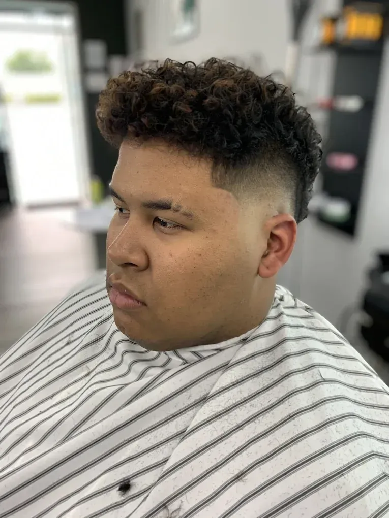 Man with curly hair and a faded haircut, wearing a barber's cape, at a salon.