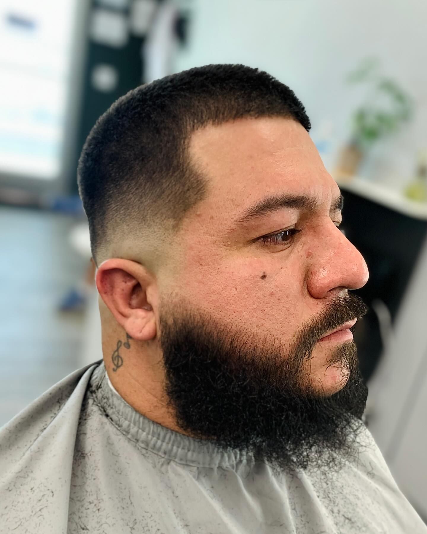 Man with a fade haircut and full beard, looking right. Blurred background of a barbershop.