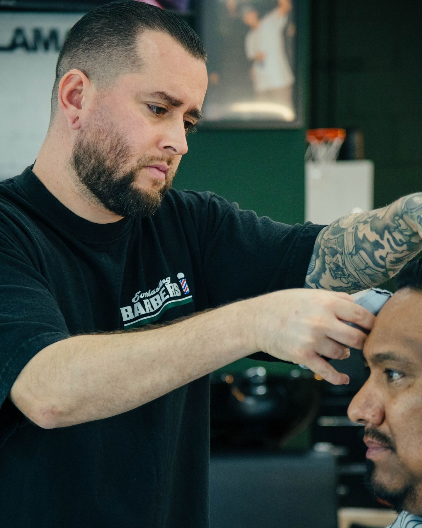 Barber using clippers to cut a customer's hair in a shop, both focused, shop in the background.
